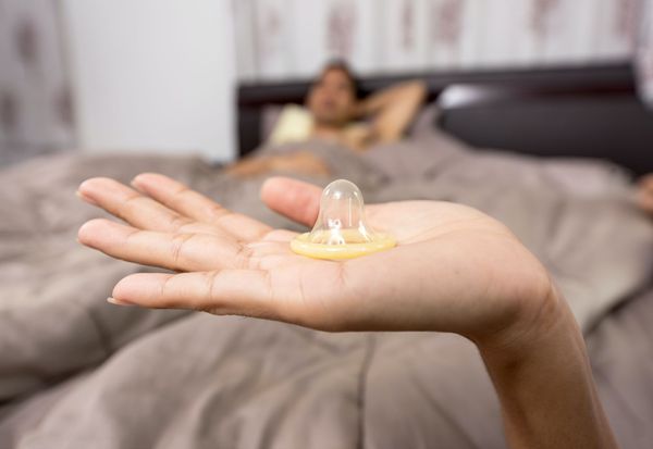A woman holding a condom and a man on the bed